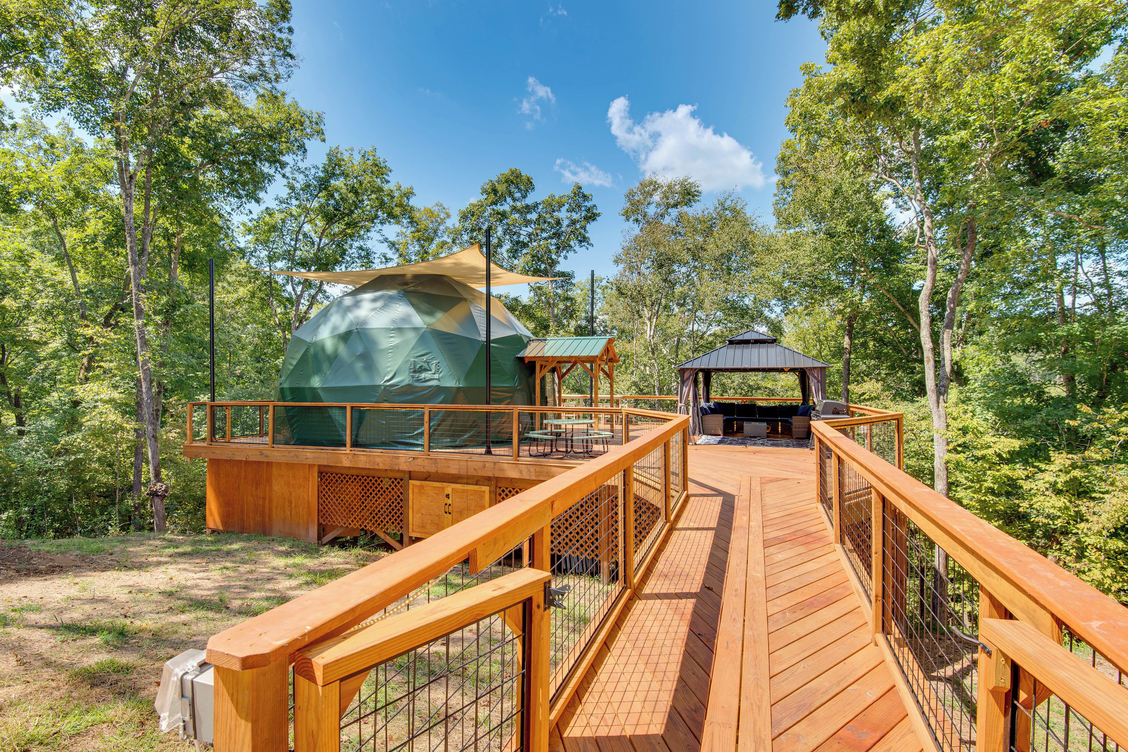 Un pontile di legno conduce a una tenda coperta e un gazebo in una zona boschiva.