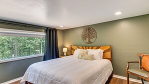 A bedroom with a large bed, a wooden headboard, a nightstand with a lamp, a chair, and a window with curtains. - Hot Tub & 2 Fire Pits! Secluded Lyles Getaway (Lyles)