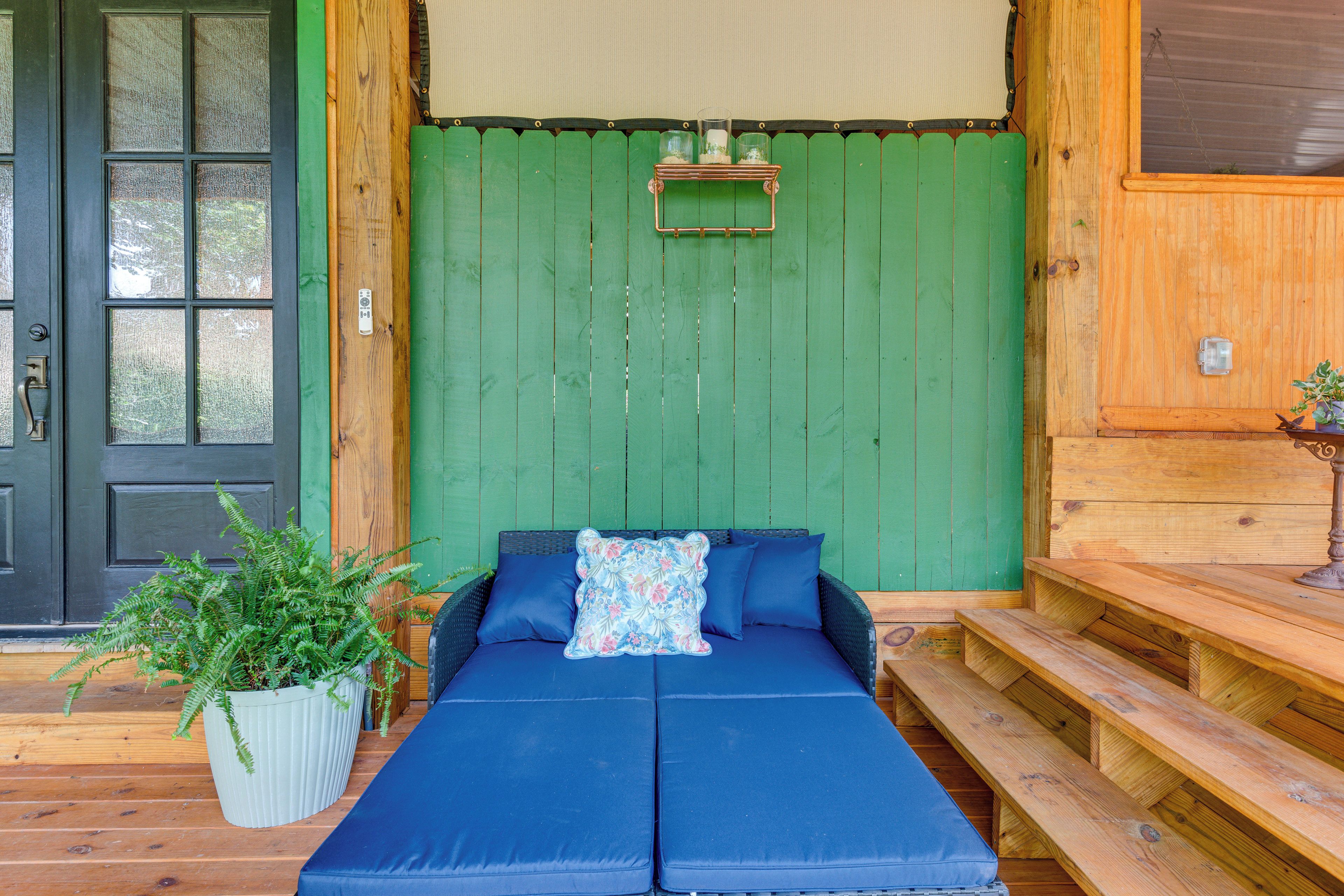 Una habitación con pared verde, puerta negra, sofá con cojines azules y una mesita con una planta.