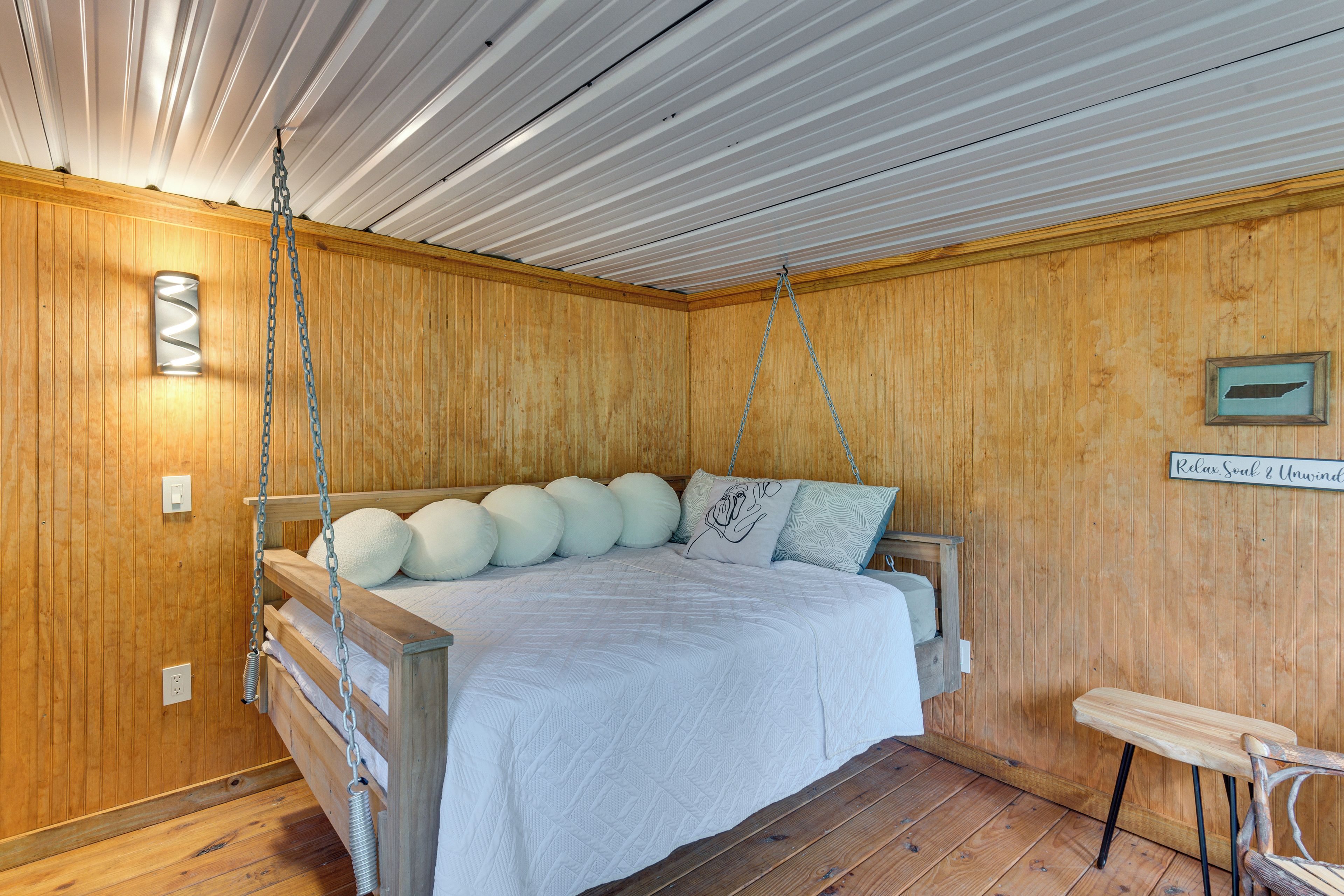 Ein Zimmer mit Holzwandverkleidung, einem Bett mit vielen Kissen und einer hängenden Leuchte.