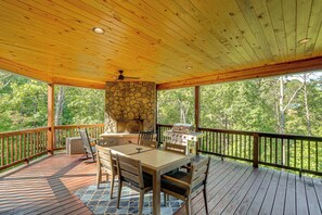 A covered outdoor deck with a stone fireplace, a grill, and a dining table with chairs. - Sauna, Hot Tub, Mtn View! Stunning Home Near Helen (Sautee Nacoochee)