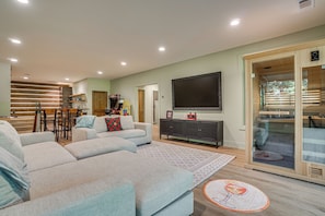 A modern living room with a sectional sofa, a flat-screen TV, and a dining area with wooden chairs. - Sauna, Hot Tub, Mtn View! Stunning Home Near Helen (Sautee Nacoochee)