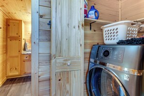 A laundry room with a front-loading washing machine, wooden walls, and a shelf with laundry supplies. - 4 Mi to Cherokee Lake! Wooded Escape Near Hiking (Murphy)