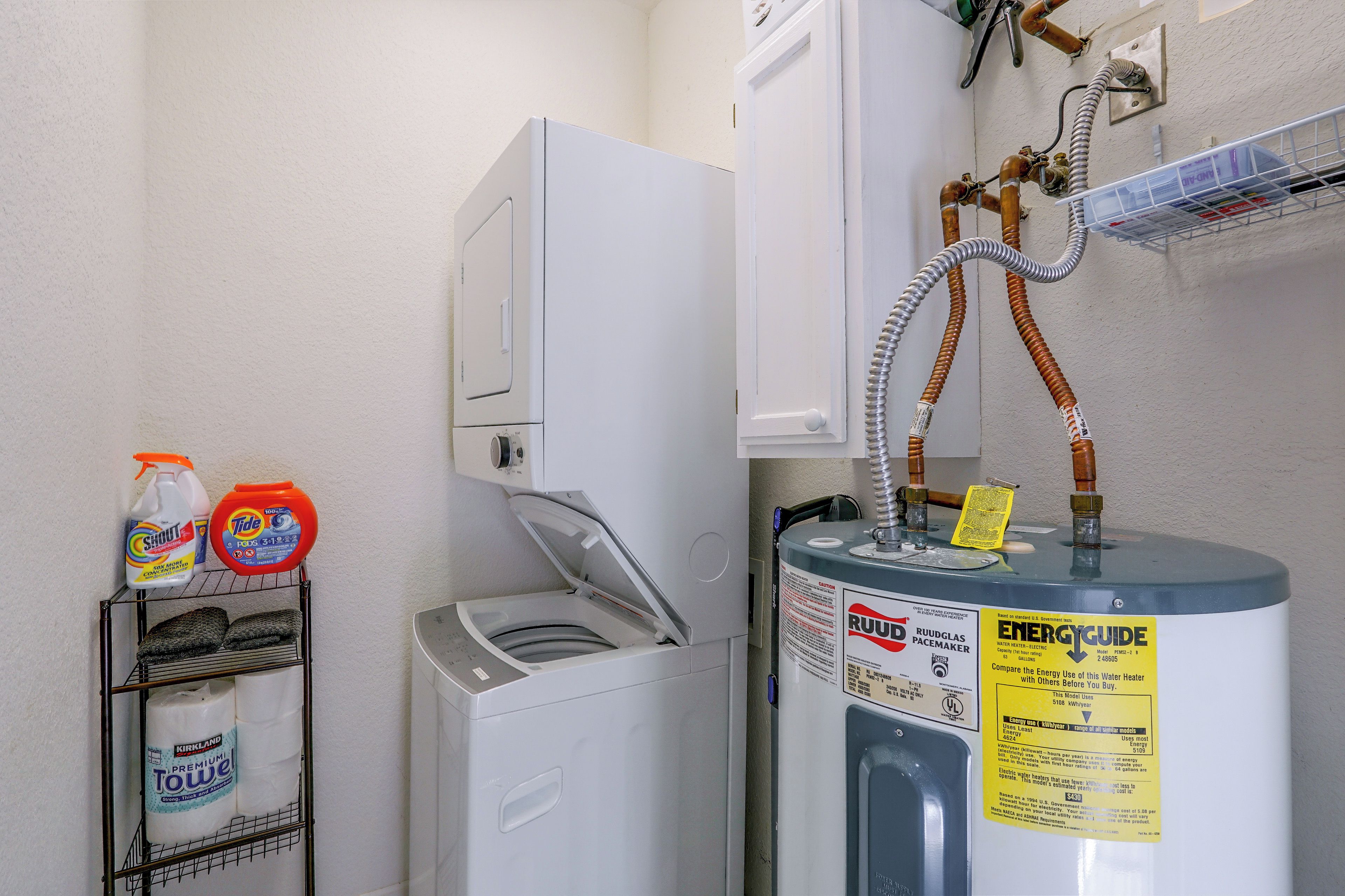 Un cuarto de servicio con calentador de agua, lavadora y estante con productos de limpieza.
