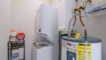 Un cuarto de servicio con calentador de agua, lavadora y estante con productos de limpieza.