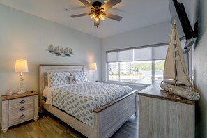 A bedroom with a bed, bedside lamps, a ceiling fan, a sailboat decoration, and a window with a view. - Pool Access! Family Getaway on Lake of the Ozarks (Lake Ozark)