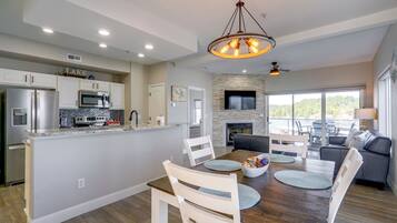 A modern kitchen with built-in appliances, a dining area with a wooden table and chairs, and a living room with a fireplace and a large window.