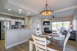 A modern kitchen with built-in appliances, a dining area with a wooden table and chairs, and a living room with a fireplace and a large window. - Pool Access! Family Getaway on Lake of the Ozarks (Lake Ozark)