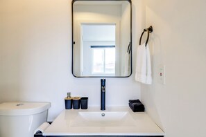 Ein Badezimmer mit einem weißen Waschbecken, einem Spiegel, einer Toilette und einem Handtuchhalter mit Handtüchern.