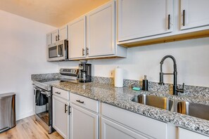 A modern kitchen with white cabinetry, a stainless steel sink, a built-in microwave, and a coffee maker. - South Tampa Stay w/ Backyard & Fire Pit! (Tampa)
