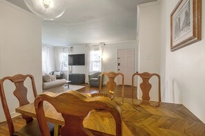 Ein Essbereich mit Holztisch und -stühlen, ein Wohnzimmer mit Sofa und Fernseher sowie ein Flur mit einer Tür.