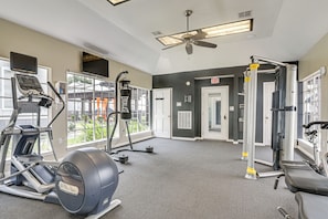 A gym with various exercise equipment, including treadmills and weight machines, and a large window providing a view of the outside.