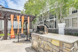 An outdoor patio area with a stone barbecue grill, wooden pergola with orange curtains, and outdoor seating.