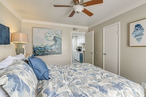 A bedroom with a bed, a ceiling fan, a painting, a lamp, and a door.