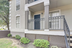 A two-story building with a front porch, a black door, and a small garden area with shrubs.