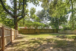 A fenced backyard with a grassy area, trees, and a wooden fence. - Near Midtown Attractions! Memphis Duplex (Memphis)