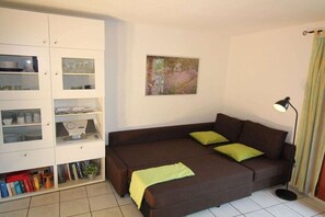 A living room with a brown sofa, green cushions, a white cabinet with glass doors, and a floor lamp. - Holiday home in Gruissan with swimming pool (Gruissan)