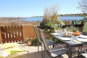 An outdoor dining area with a table set for two, chairs, and a view of a lake. - Holiday home in Gruissan with swimming pool (Gruissan)