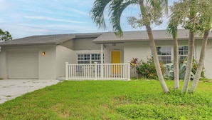 A single-story house with a garage, a front porch with a railing, and a small garden with palm trees and shrubs. - Hot Tub, Water View! Largo Home 10 Mi to Beaches (Largo)