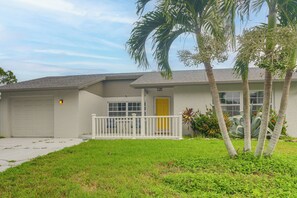 Einbungalow mit Garage, einer Veranda mit Geländer und einem kleinen Garten mit Palmen und Sträuchern.