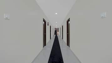 Un couloir d’hôtel avec un tapis noir, des murs blancs et des portes de chaque côté.