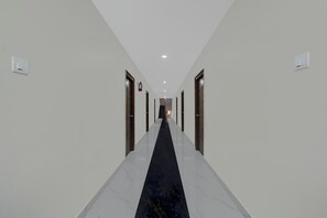 A hotel corridor with a black carpet, white walls, and doors on both sides. - Townhouse Oak Bachupally Medical College (Hyderabad)