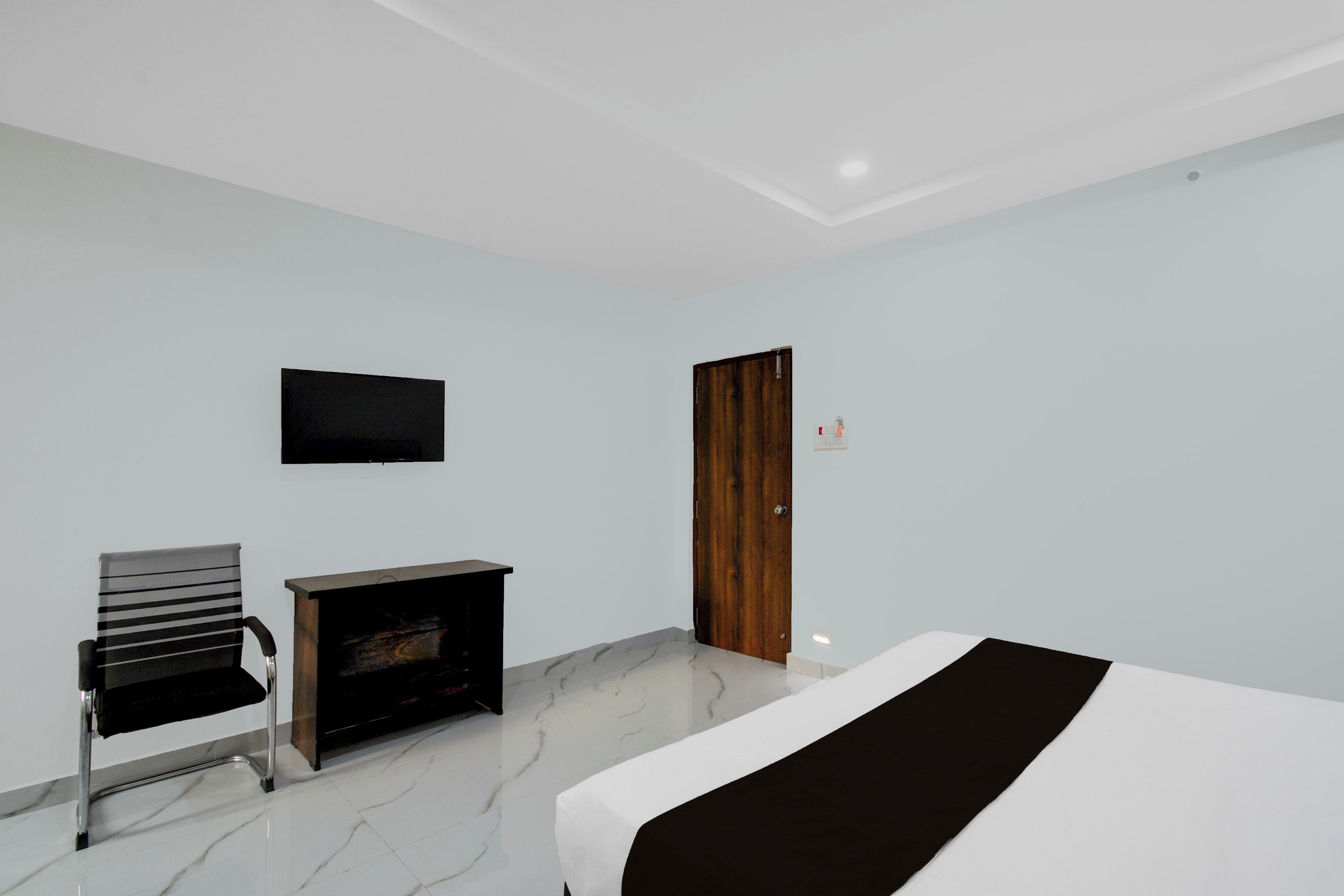 A hotel room with a bed, a TV mounted on the wall, a wooden door, and a chair.