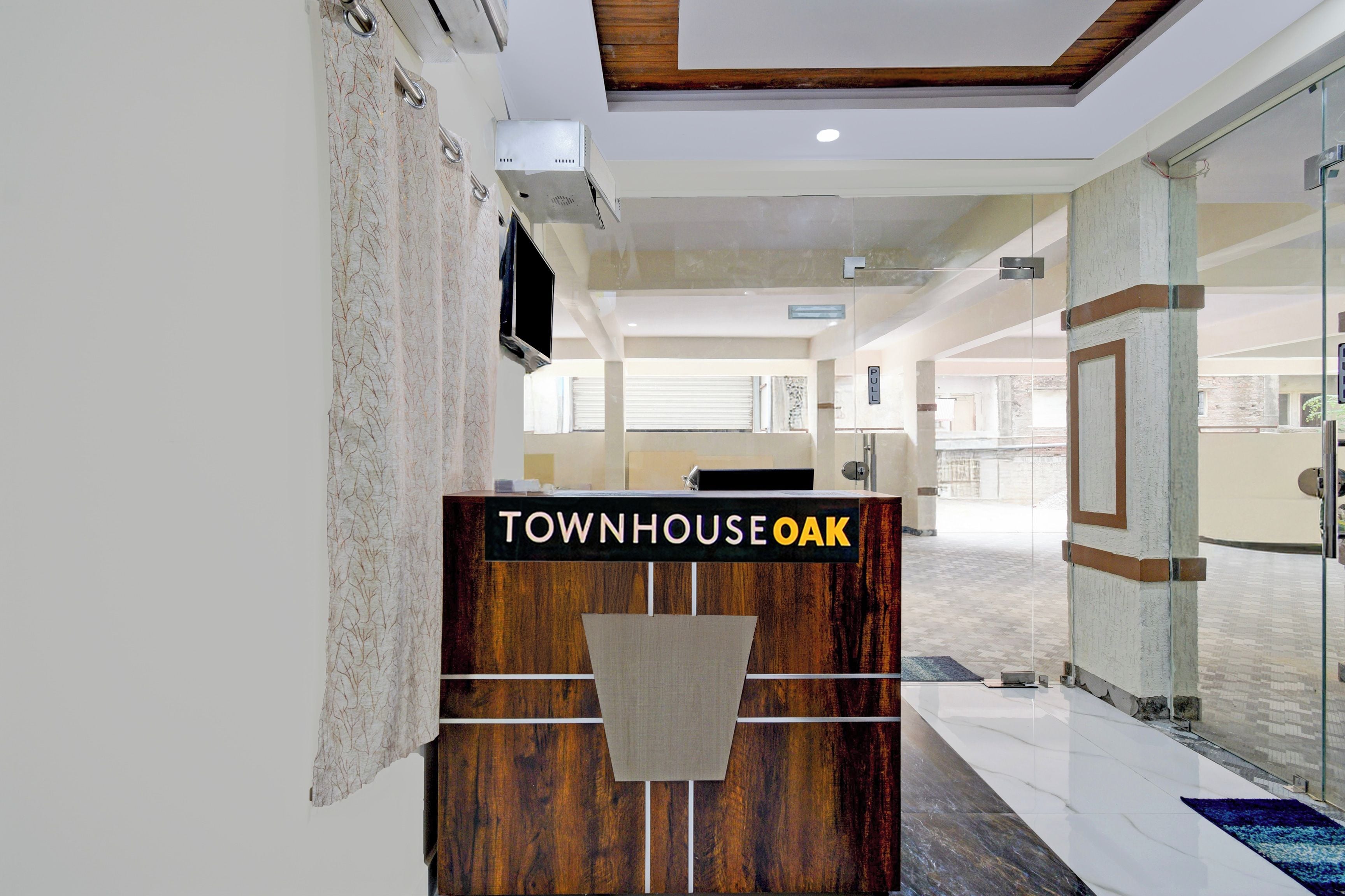 Un mostrador de recepción con un cartel que dice 'TOWNHOUSE OAK' en un vestíbulo moderno con puertas de vidrio y suelo de baldosas.