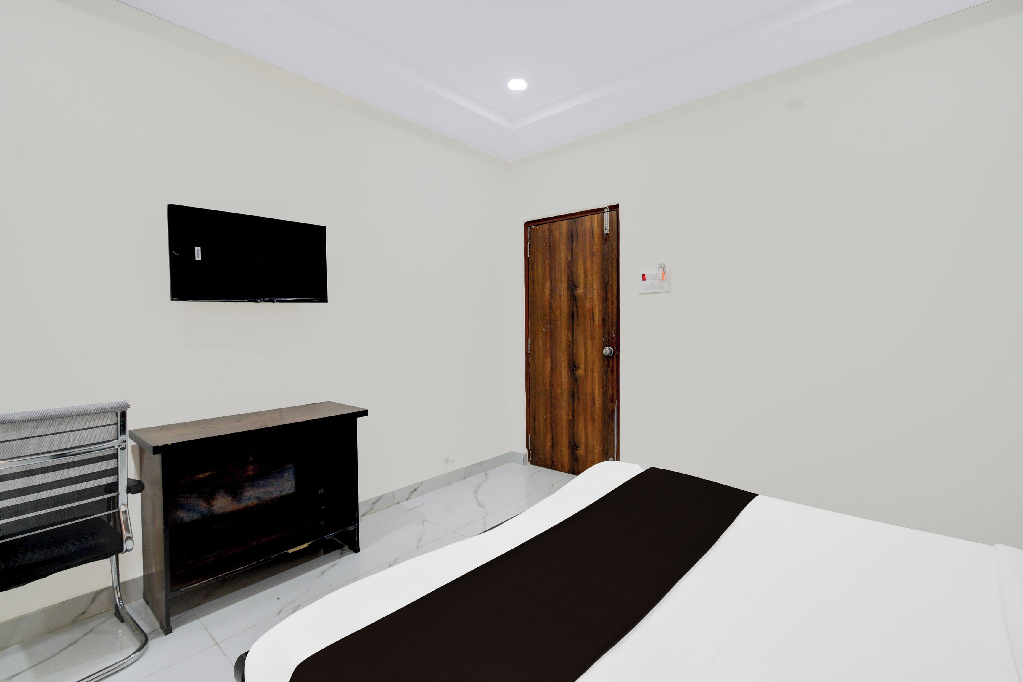 Un dormitorio con una cama, un televisor montado en la pared, una puerta de madera y un banco con televisor.
