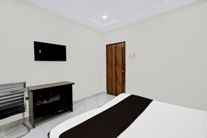 Un dormitorio con una cama, un televisor montado en la pared, una puerta de madera y un banco con televisor.