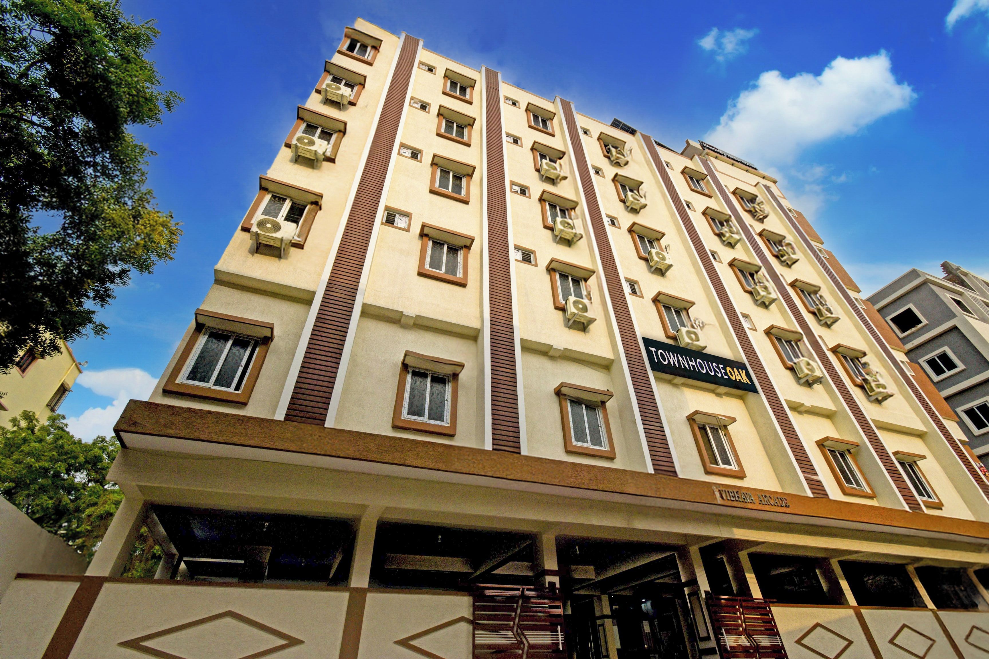 Un hotel de varios pisos con una entrada central, balcones y un letrero que indica 'TOWNHOUSE OAK' en la fachada.