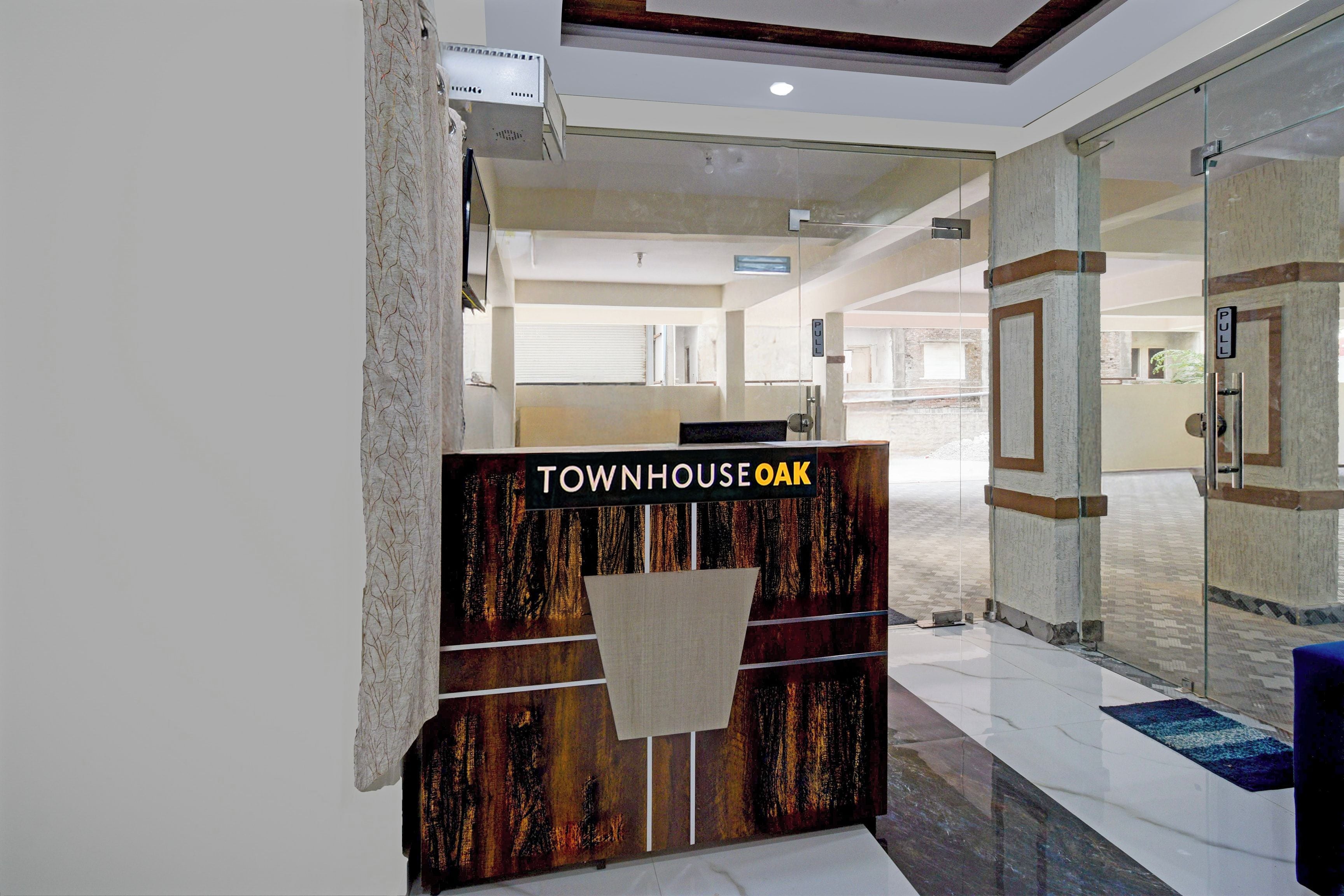 Un mostrador de recepción con un letrero que dice 'TOWNHOUSE OAK' en un vestíbulo moderno con puertas de vidrio y piso de baldosas.