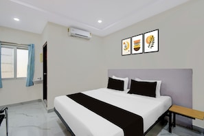 A hotel room with a bed, a bedside table, a window with curtains, an air conditioning unit, and three framed artworks on the wall. - Townhouse Oak Bachupally Medical College (Hyderabad)