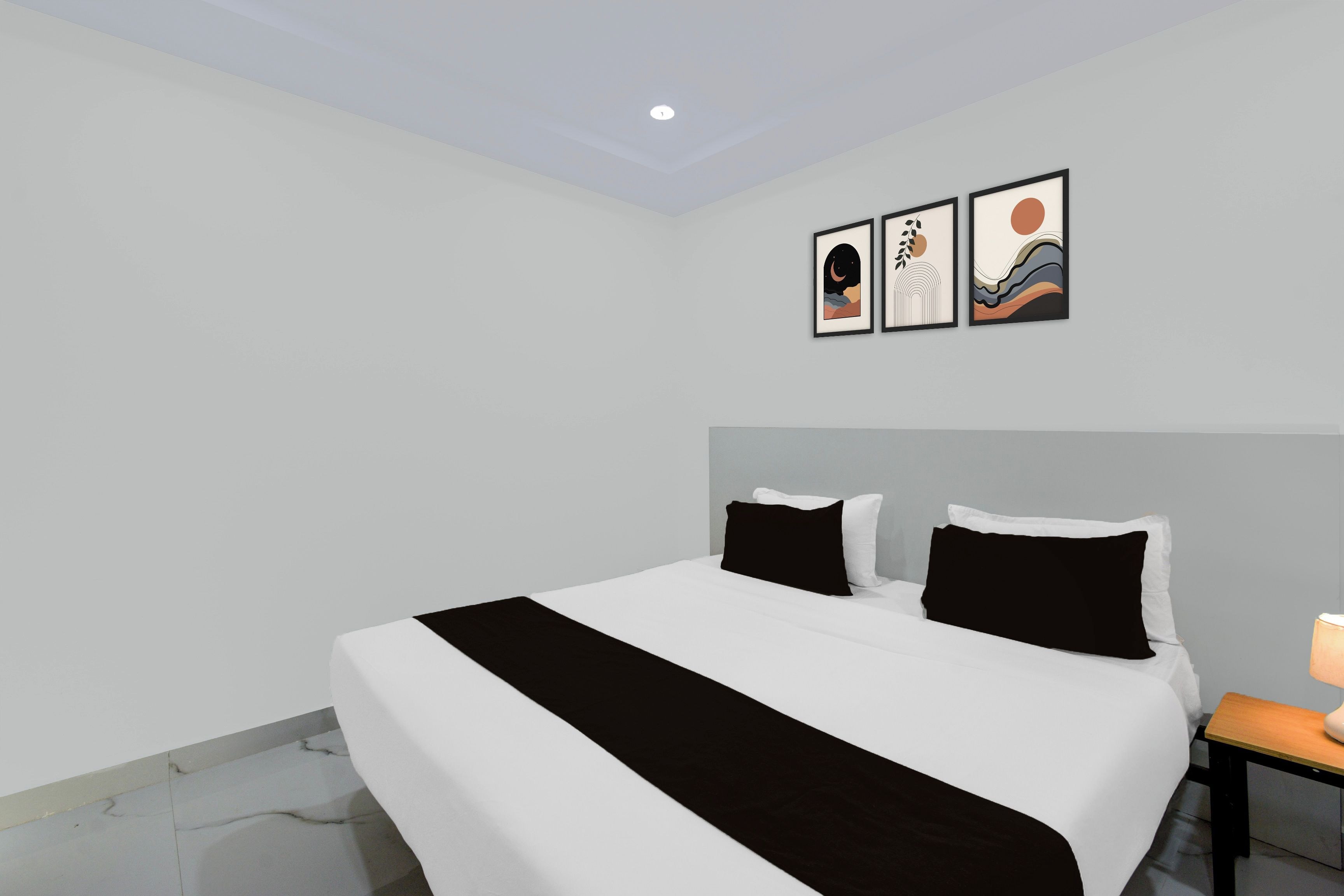 Una habitación de hotel moderna con una cama grande, dos almohadas, una mesita de noche con lámpara y tres cuadros enmarcados en la pared.