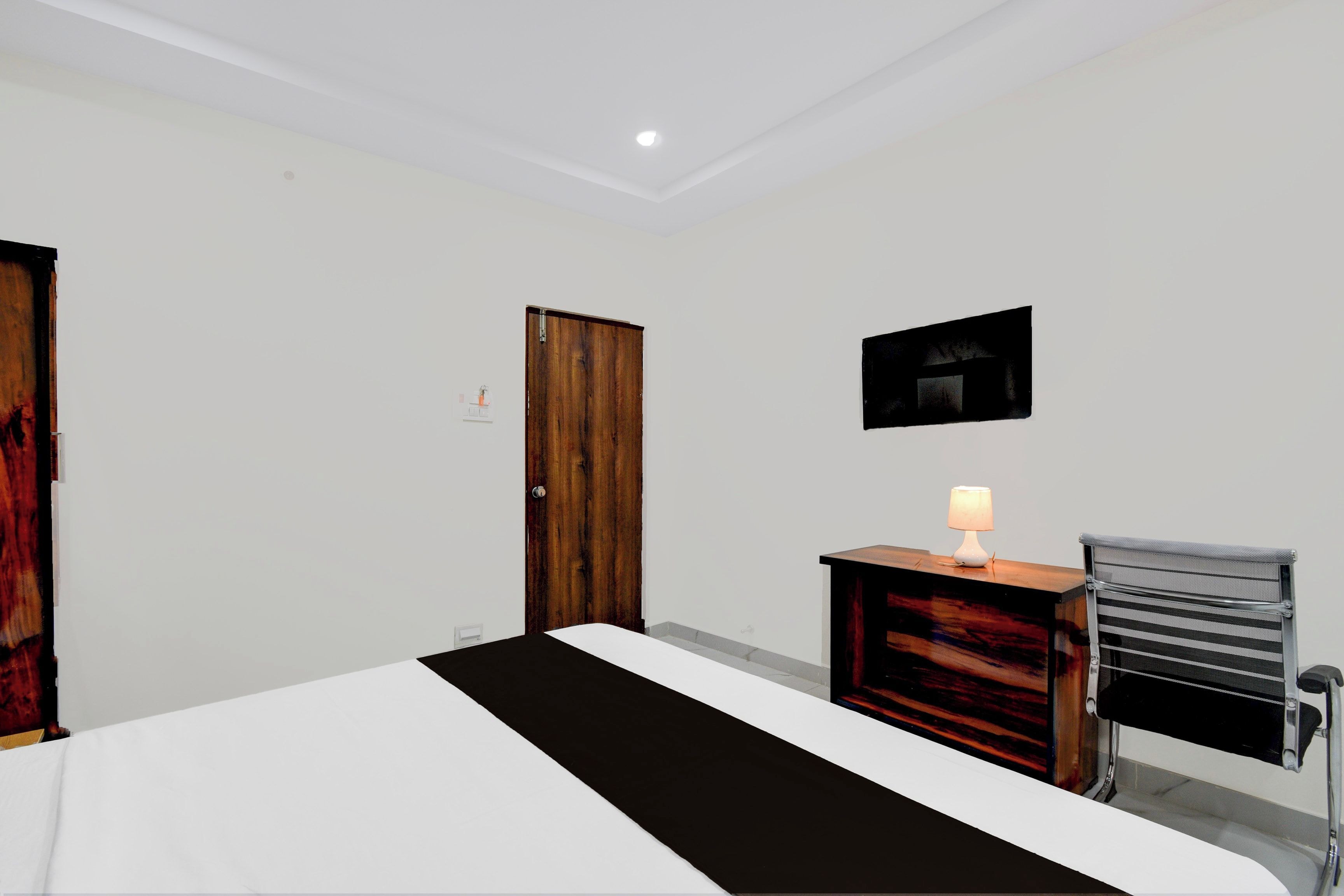 Una habitación de hotel con cama, escritorio con lámpara, una silla y una puerta.