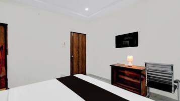 Una habitación de hotel con cama, escritorio con lámpara, una silla y una puerta.