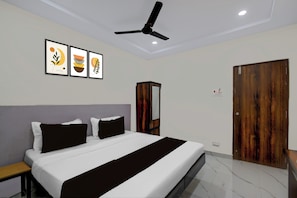 A bedroom with a bed, a ceiling fan, a wooden wardrobe, and framed artwork on the wall. - Townhouse Oak Bachupally Medical College (Hyderabad)