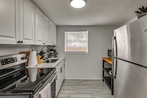 A compact kitchen with white cabinets, a stainless steel refrigerator, a built-in oven, and a window with blinds. - South Tampa Apt Near MacDill & Bayshore (Tampa)