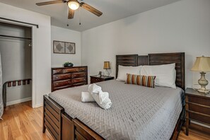 A bedroom with a wooden bed, a nightstand, a dresser, a ceiling fan, and a wall-mounted artwork. - South Tampa Apt Near MacDill & Bayshore (Tampa)
