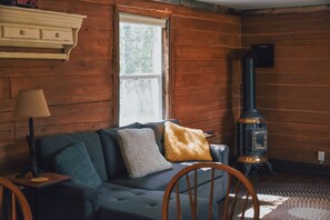 A cozy living room with a sofa, a lamp, and a wood-burning stove. - Mtn Views & Trail Access! Driggs Couple's Getaway (Driggs)