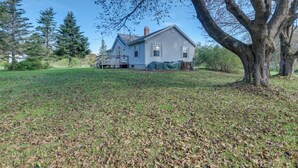 A two-story house with a covered porch and a large tree in the foreground. - 21 Acres, Near Trails to Shore with Island Access (Lubec)