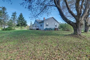 A two-story house with a covered porch and a large tree in the foreground. - 21 Acres, Near Trails to Shore with Island Access (Lubec)
