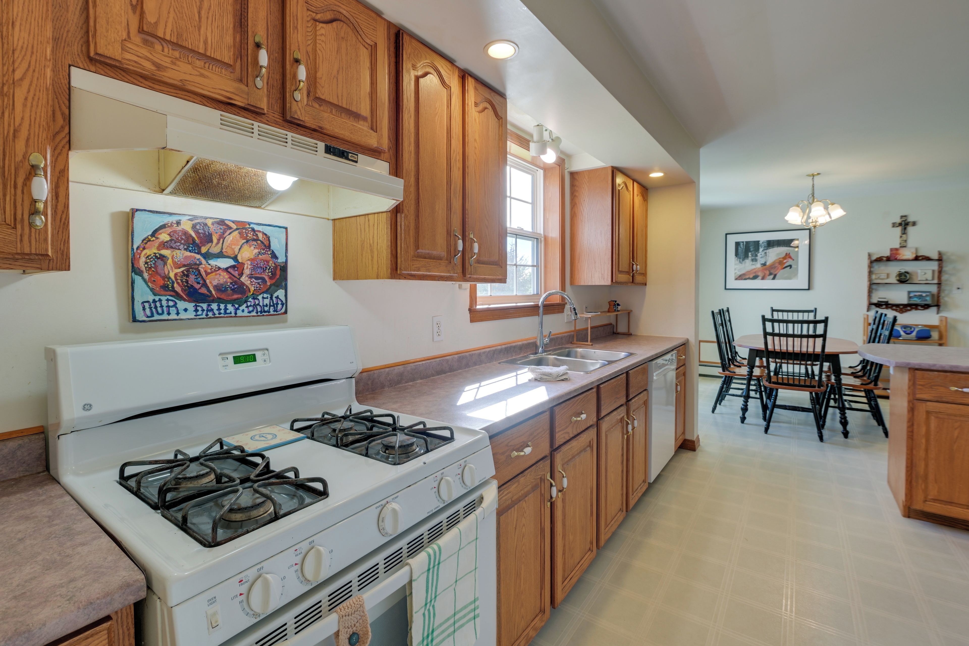 A kitchen with wooden cabinets, a gas stove, a sink, and a dining area with chairs and a table.