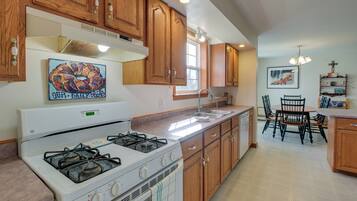 A kitchen with wooden cabinets, a gas stove, a sink, and a dining area with chairs and a table.
