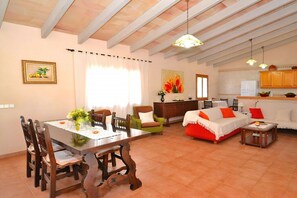 A spacious living area with a dining table, chairs, a sofa, and a kitchen in the background.