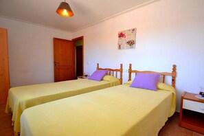 A room with two single beds, wooden headboards, a nightstand with a lamp, a wall clock, and a door.