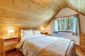 Ein Schlafzimmer mit Holzboden, einem Bett mit weißer Bettwäsche, zwei Nachttischlampen, einem Fenster mit Vorhängen und einem Nachttisch aus Holz.
