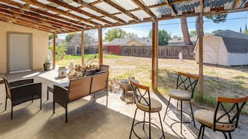 Eine überdachte Terrasse mit Tisch und Stühlen, einer Feuerstelle und Blick auf einen Garten.