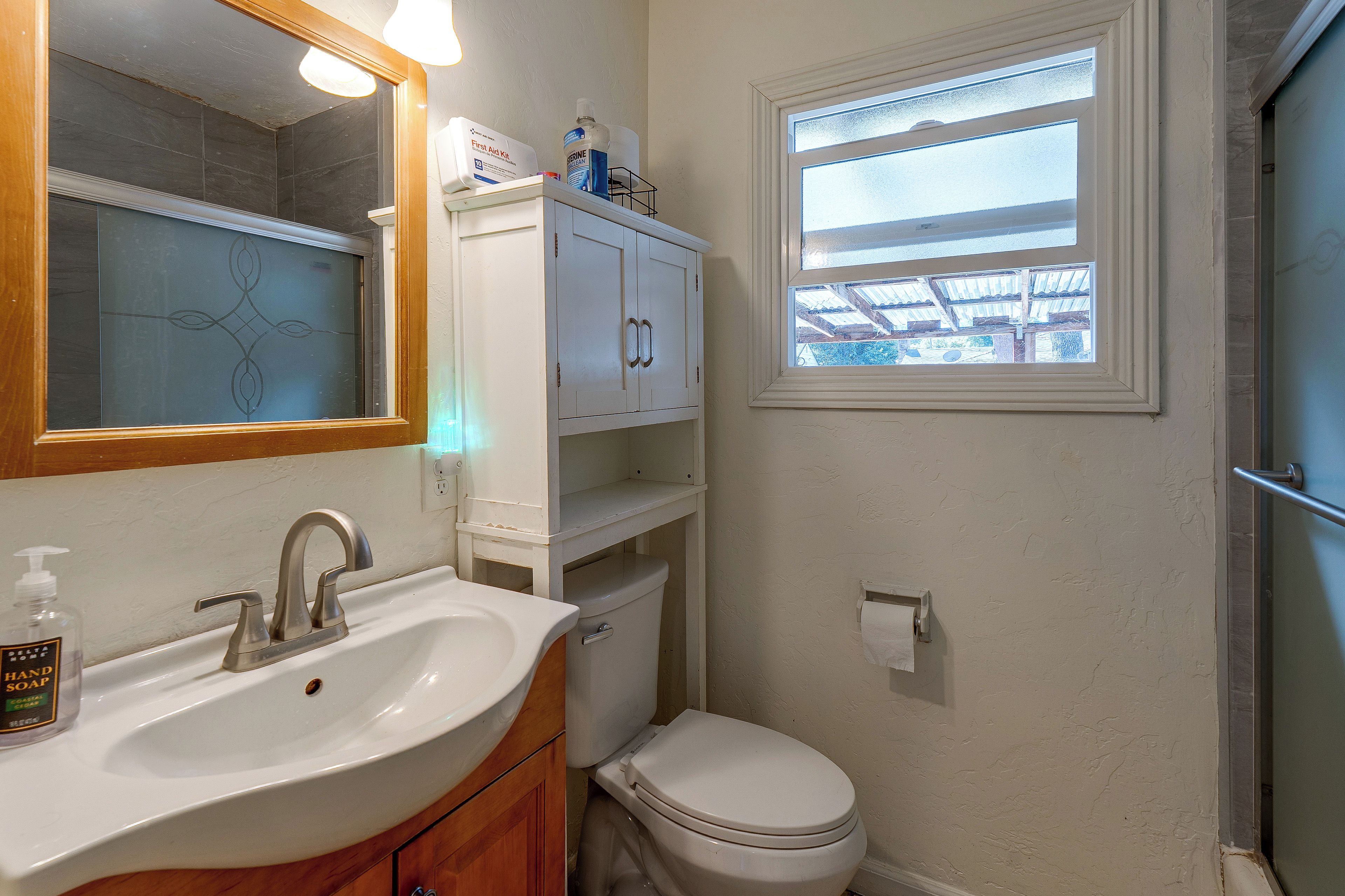 A bathroom with a white sink, a mirror, a toilet, and a window.