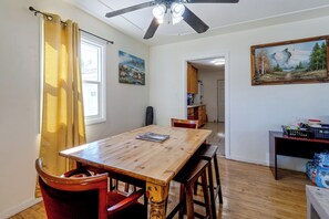 A dining area with a wooden table and chairs, a ceiling fan, and artwork on the walls.